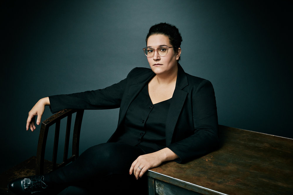 Queer Author Carmen Maria Machado 
sitting down leaning against desk 