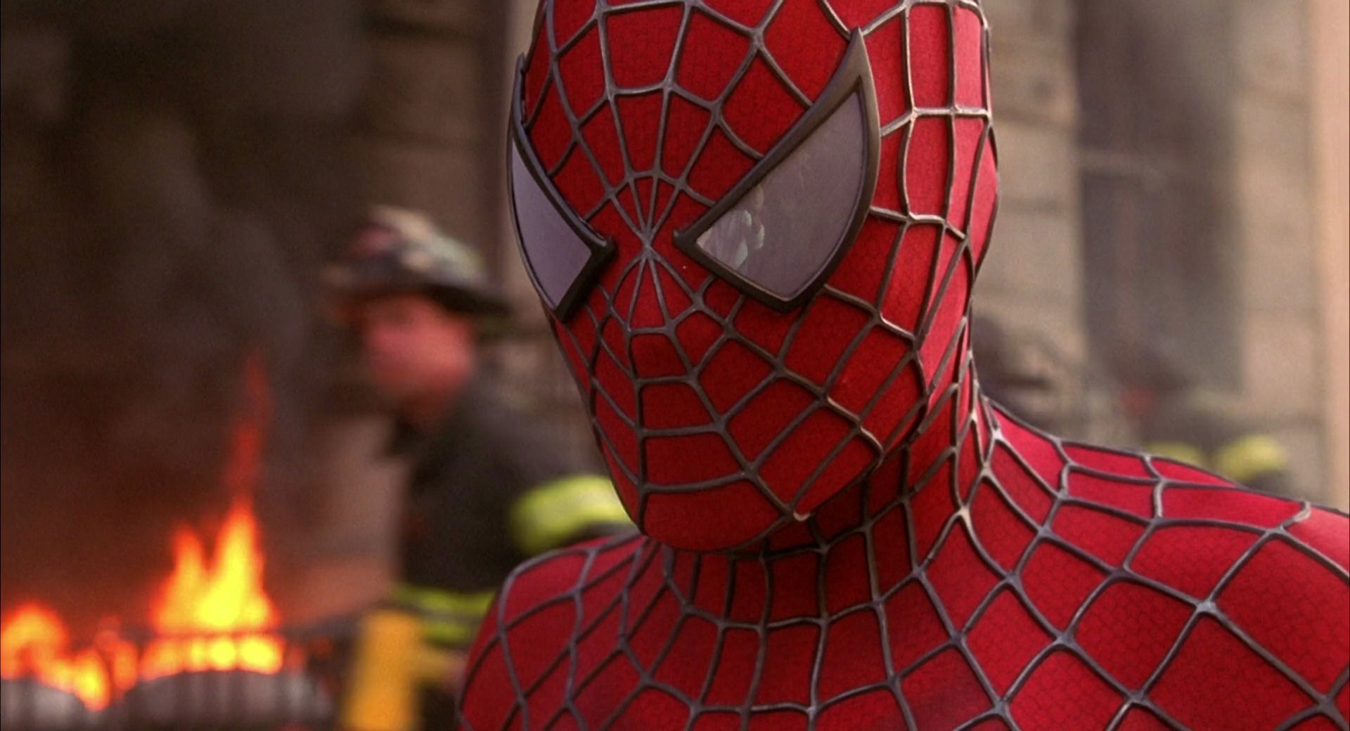 Spider-Man stands in front of a burning building, a fireman walking behind.