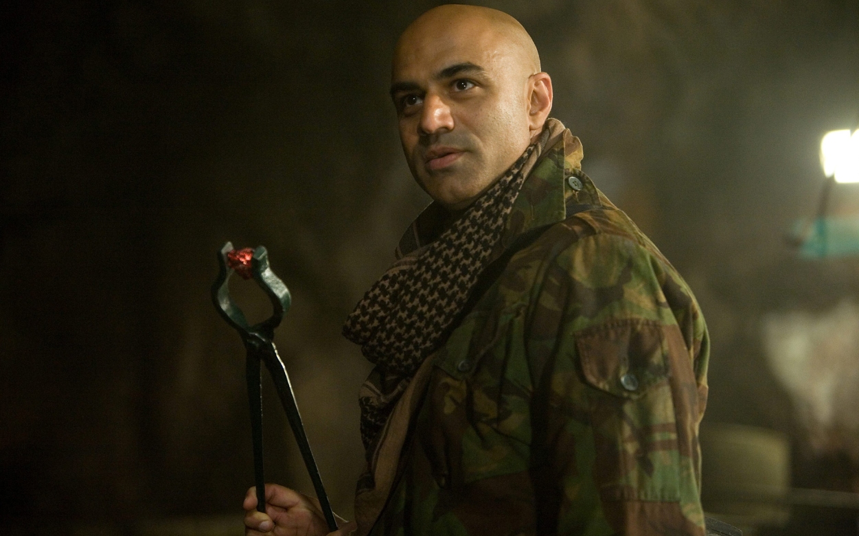 Raza, the leader of the terrorist organization Ten Rings, holds a hot coal with metal tongs.