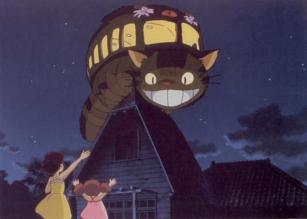 One of the Studio Ghibli cats, Catbus, smiles widely from a rooftop as Mei and Satsuki wave to him from below.