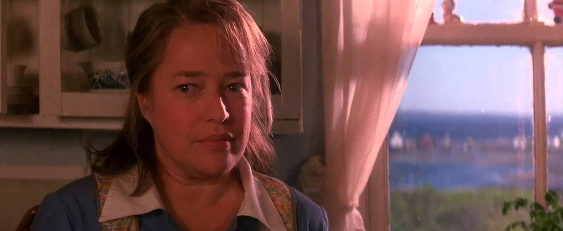 Dolores, an iconic Stephen King character, stands in front of a window, staring offscreen.