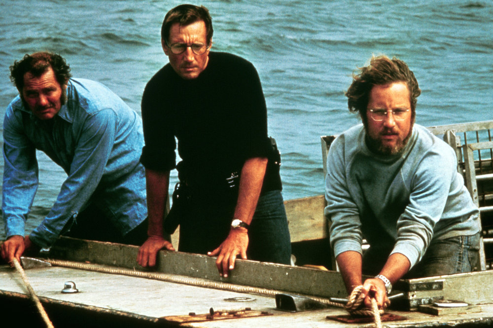 Three men are perched on a boat in the ocean looking off-camera.