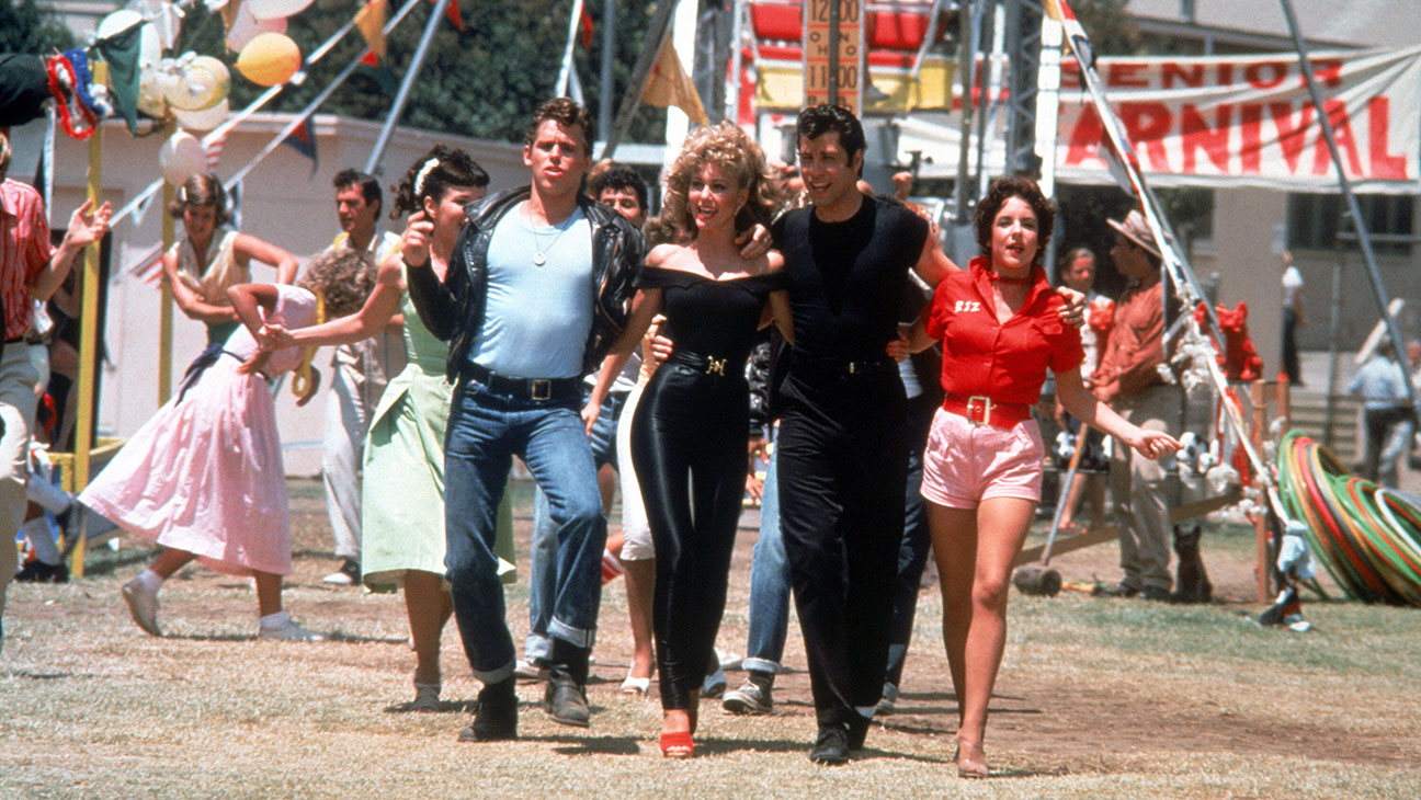 The group of main characters dances though the outdoor carnival dressed in 1960s attire.