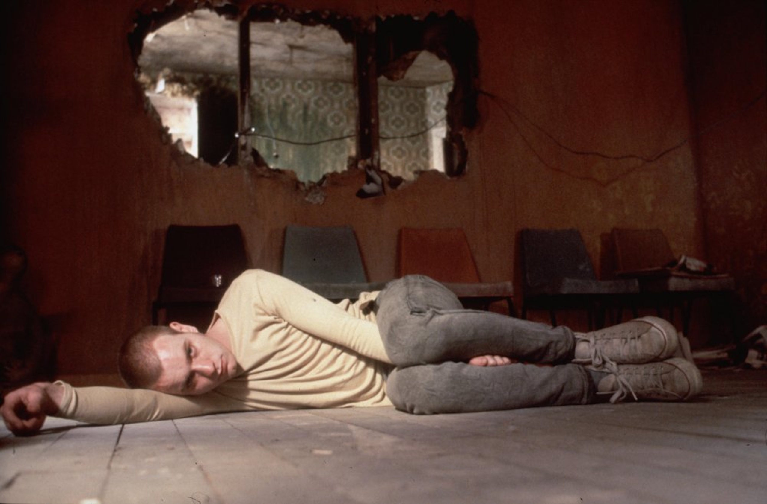Ewan McGregor's character, Renton, lying on the floor curled up. He's in a decaying abandoned building.