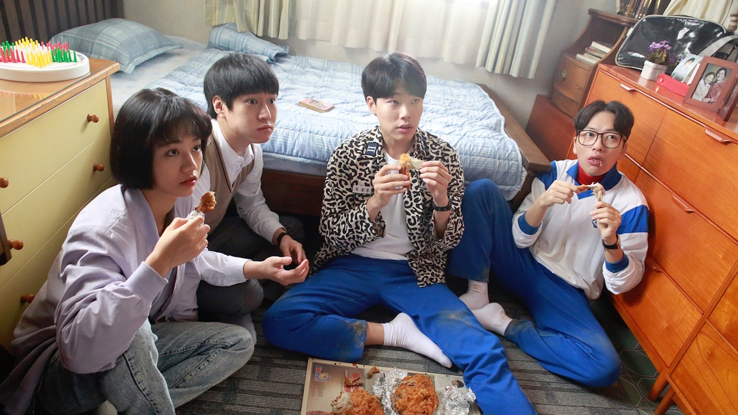 Four of the five friends from Reply 1988 sitting on the floor eating chicken
