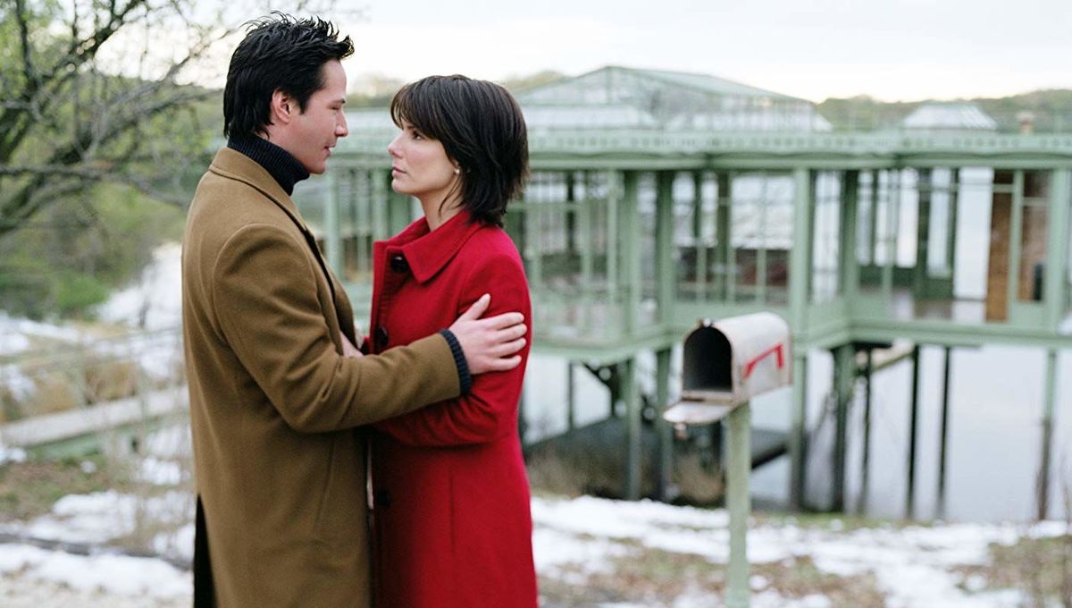 The main couple embraces while in front of a mailbox and house on the lake.