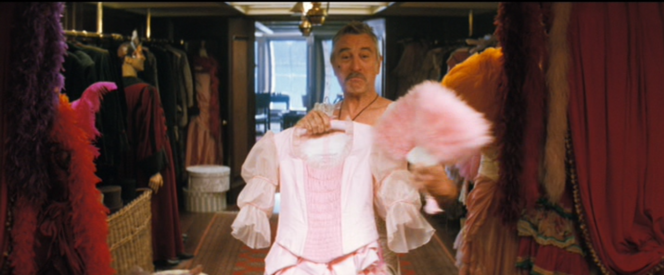 Captain Shakespeare (played by Robert De Niro) is in his closet. He is holding a pink dress and a pink fan up to his body, and he is clearly enjoying himself.