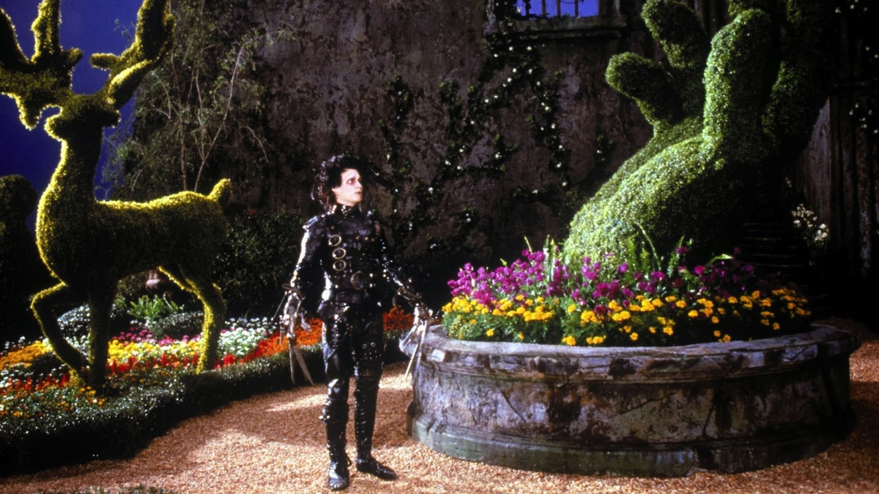 Edward Scissorhands stands in his garden, surrounded by large hedge sculptures.