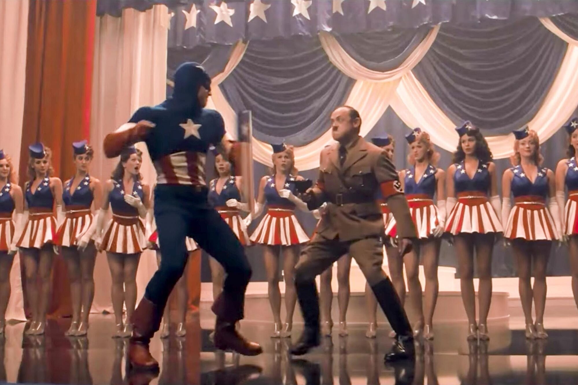 Captain America swings a fake punch at an actor playing Hitler in a stage production.