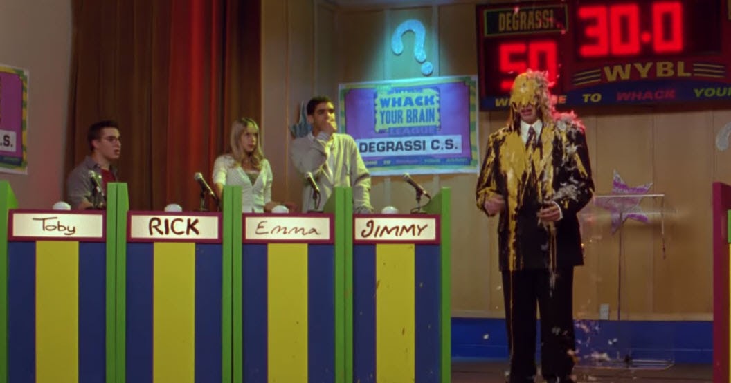 Rick stands on stage covered in yellow paint and feathers after his team wins the Degrassi academic game show.