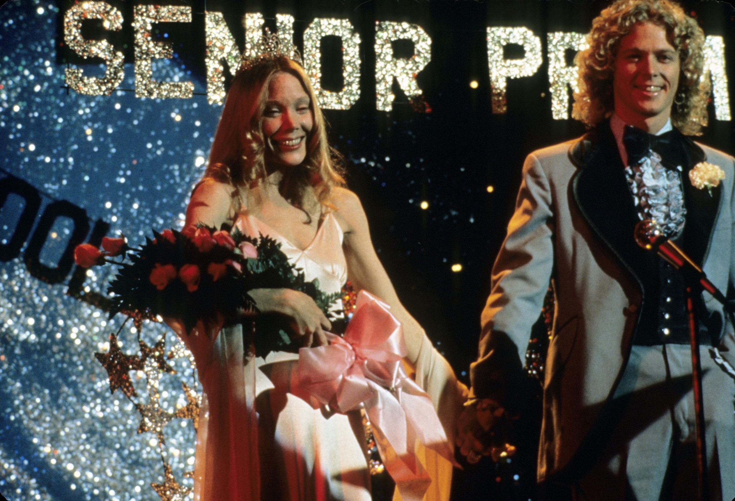 Carrie smiles, holding a bouquet of flowers at prom in Stephen King's iconic horror story.