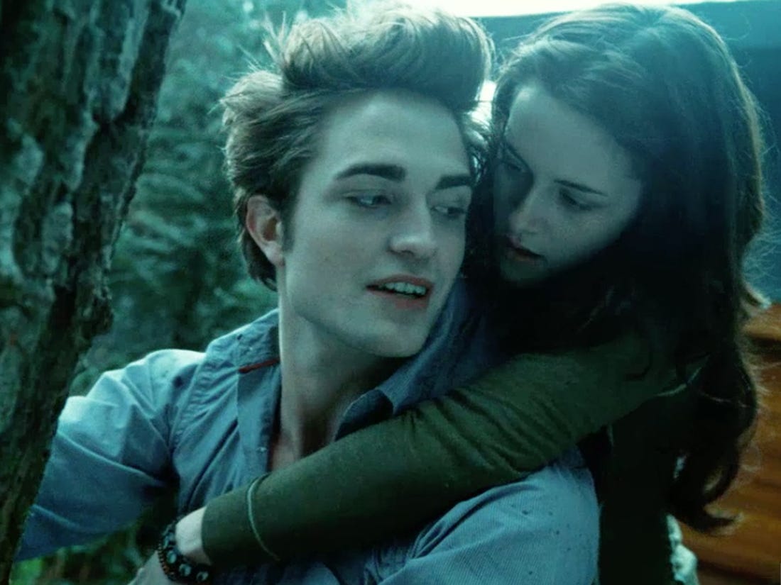 Bella Swan piggybacking off of Edward Cullen as he is about to climb a tree. 