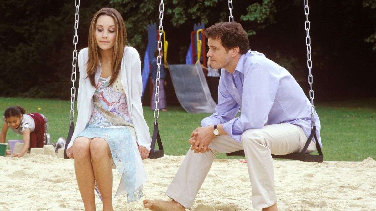 The father and daughter pair sit on an outdoor playground swing set while having a conversation.