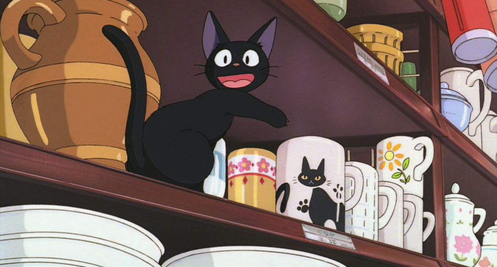 Jiji, a black cat, smiles and points his paw at a cup with a black cat on it in Kiki's Delivery Service.