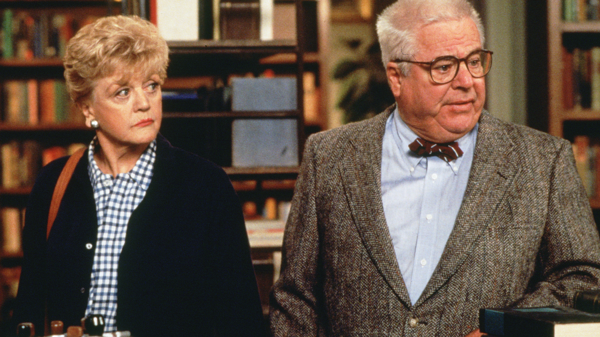 Jessica Fletcher and Doc Hazlitt in Murder, She Wrote, stand next to each other in a library.