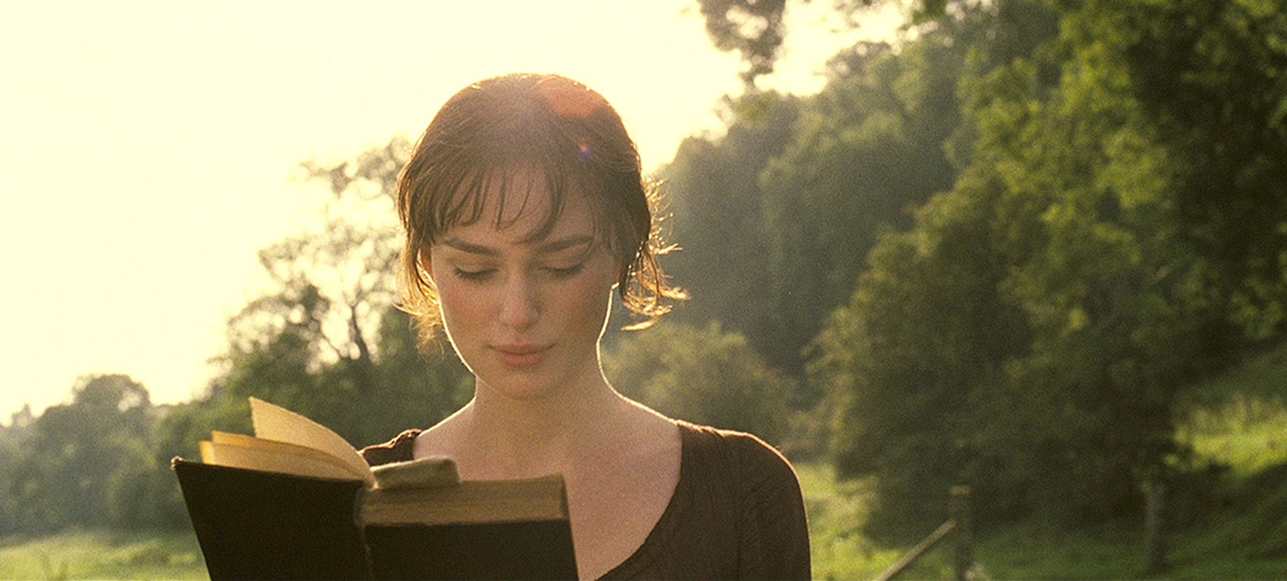 Elizabeth Bennet is reading a book while on a walk with the sun giving her a warm glow. 