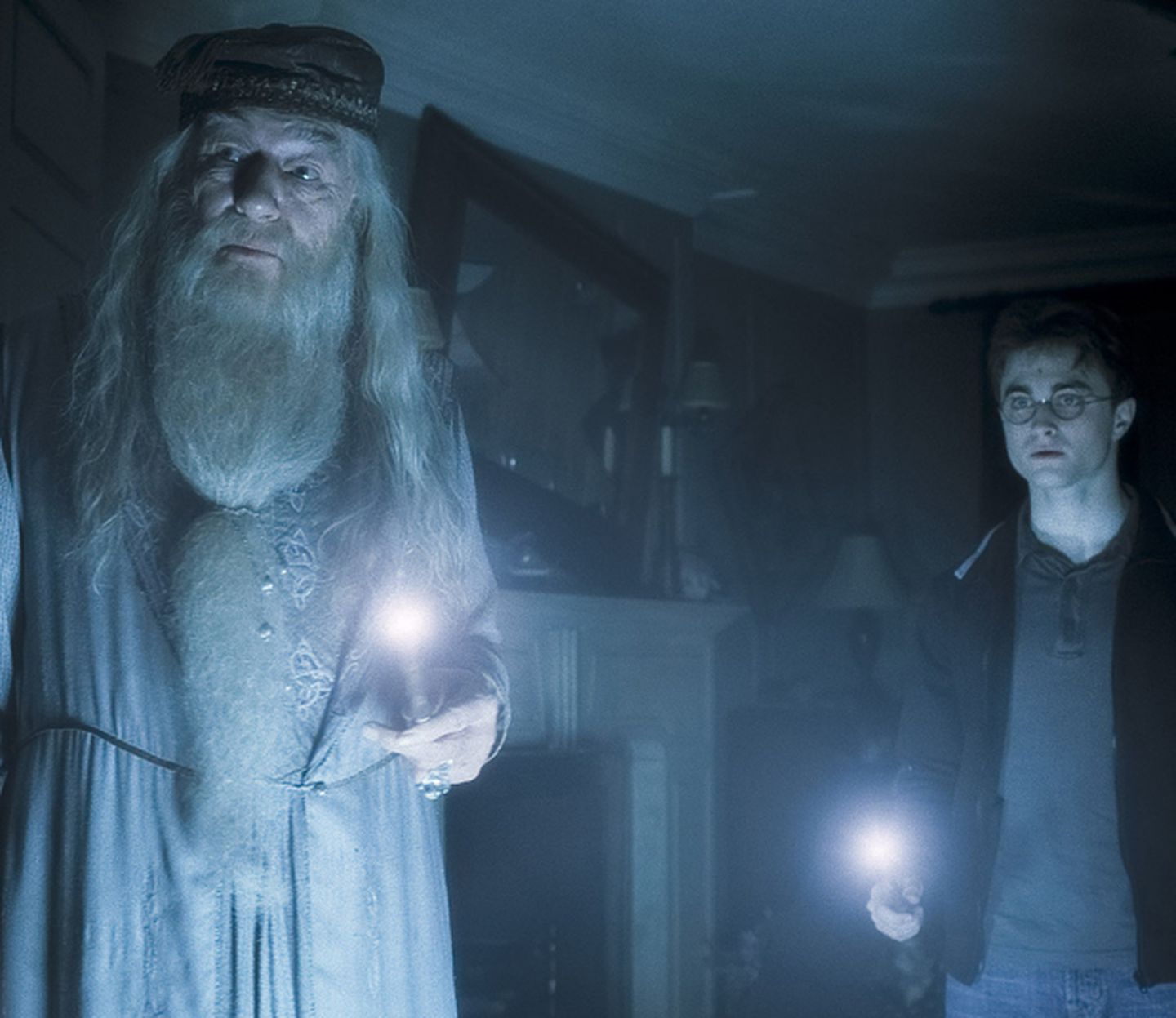 Dumbledore and Harry Potter stand in a dark room with wands alight.