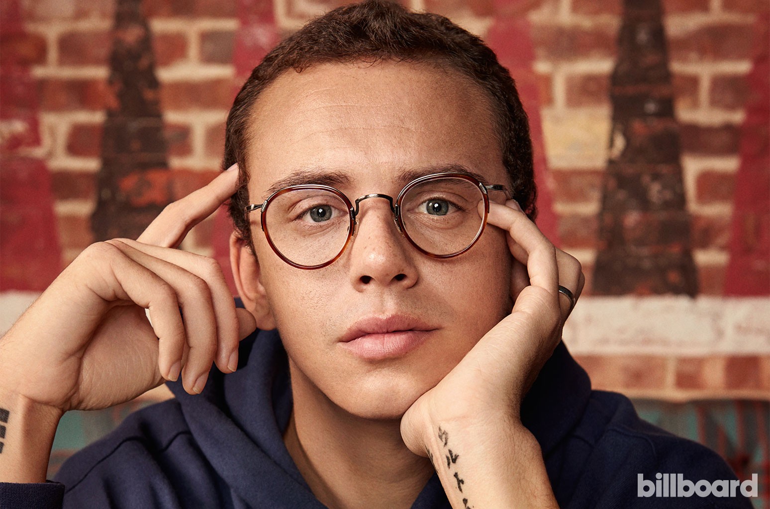 Logic staring into the camera, exposing his tattoos. 