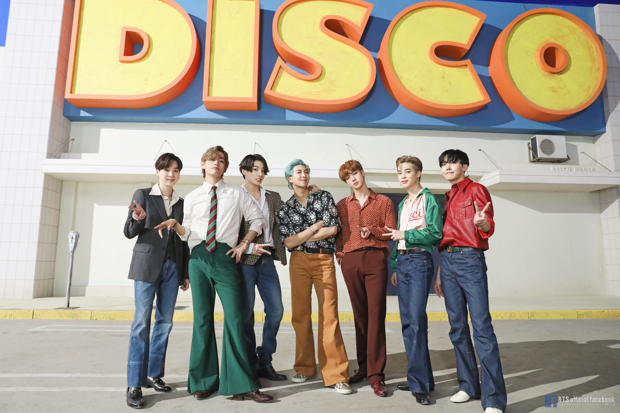 BTS posing in front of a sign that says "disco" in big letters.