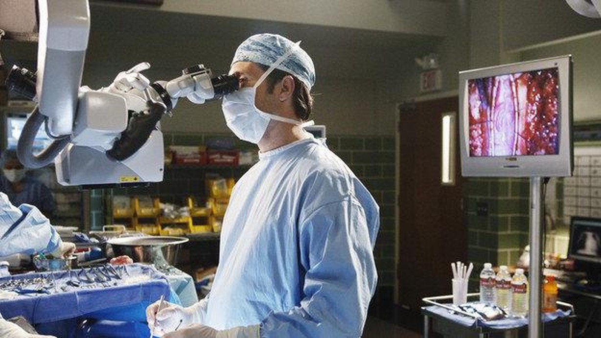 Dr. Shepard, dressed in blue scrubs operates on a patient's brain in Grey's Anatomy.