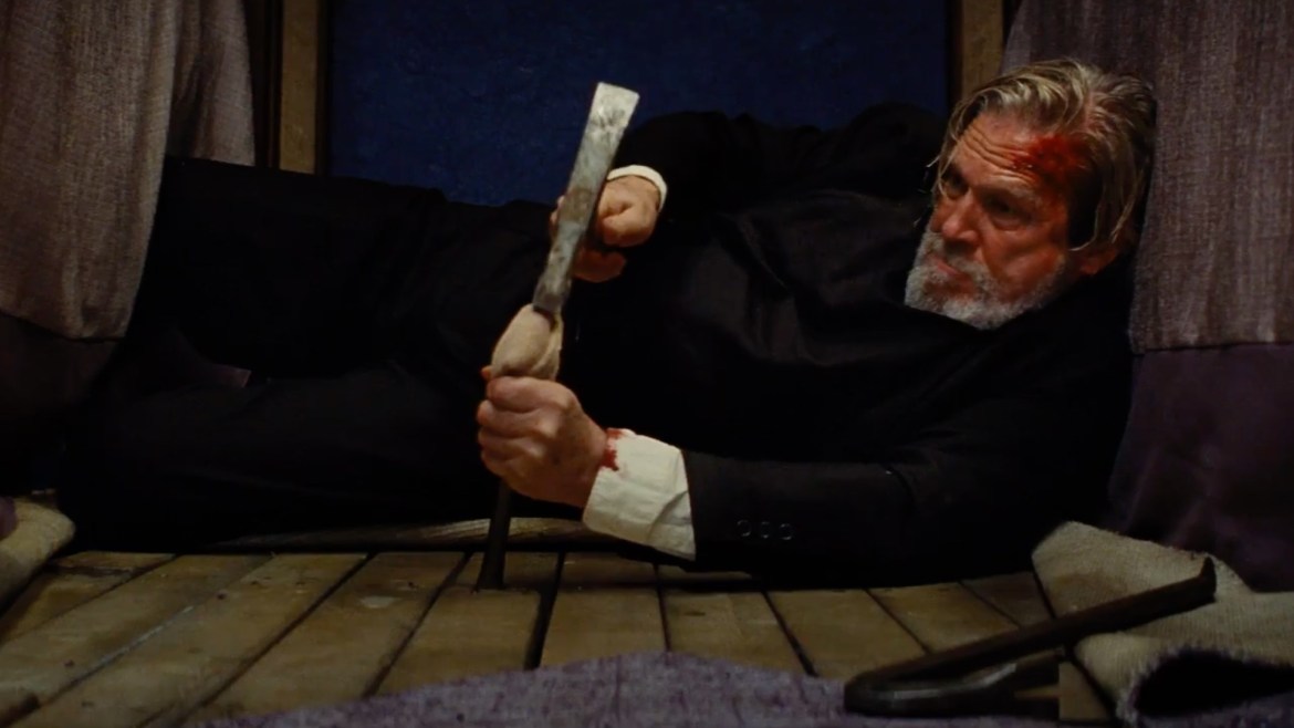 Dock O'Kelly, dressed as Father Daniel Flynn, lies on his side prying up floor boards in a hotel room.