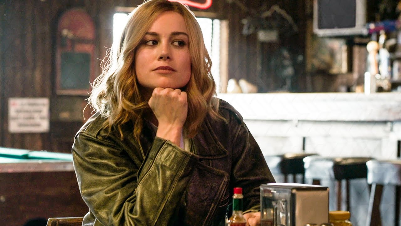 Carol Danvers rests her chin on her fist at a table in a bar.