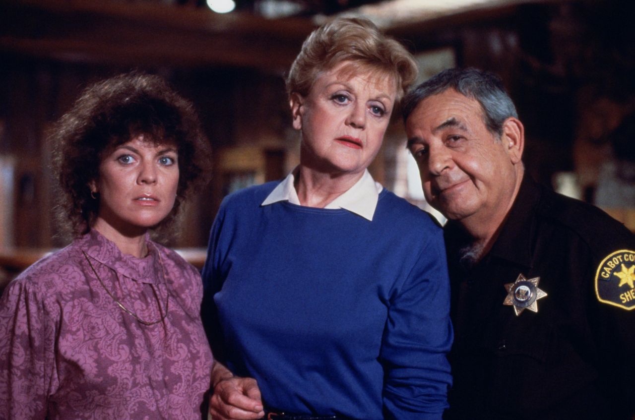 Jessica Fletcher holds the hand of a guest star while she stands next to Sheriff Tupper in Murder, She Wrote.