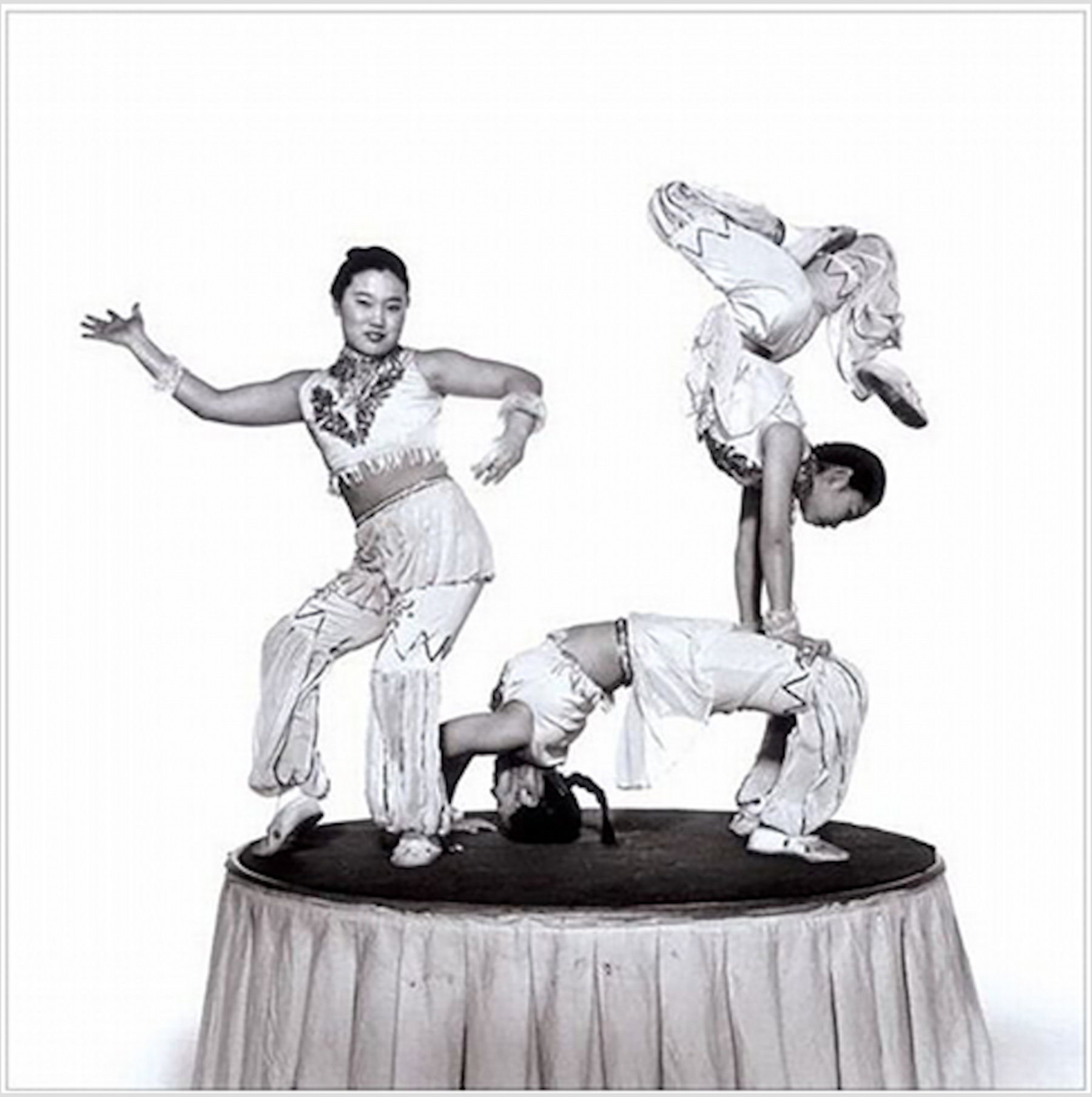 The cover for the fourth album has three acrobats. One is posing on the left side. The second is in a back bridge while the third does a handstand on their thighs. 