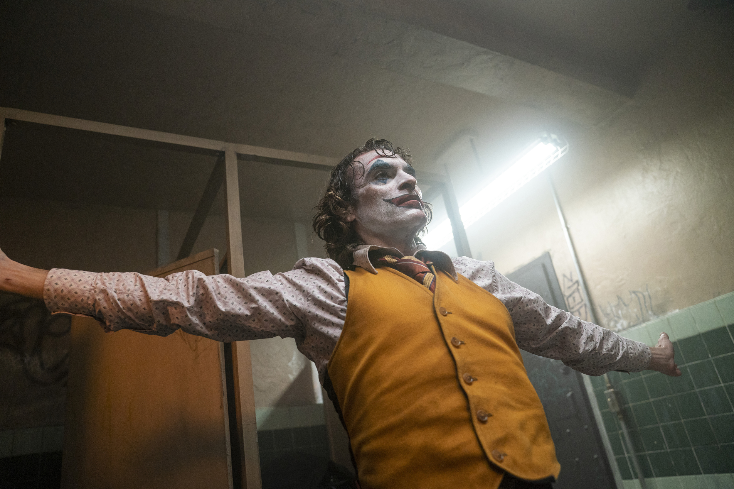 Joker stands in a bathroom, arms outstretched.