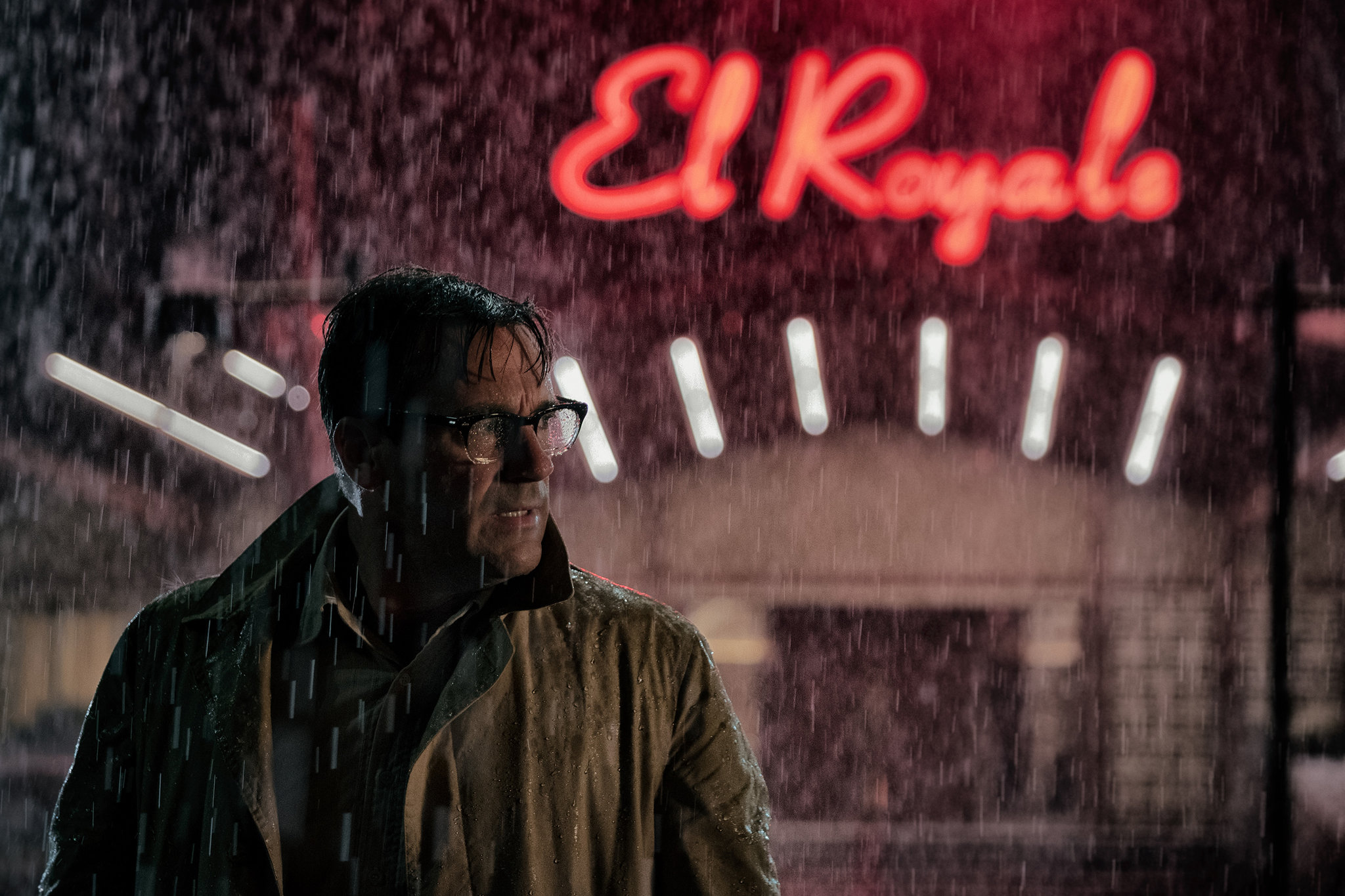 Jon Hamm as Dwight Broadbeck in Bad Times At The El Royale, stands in the rain in front of a lit up El Royale sign.