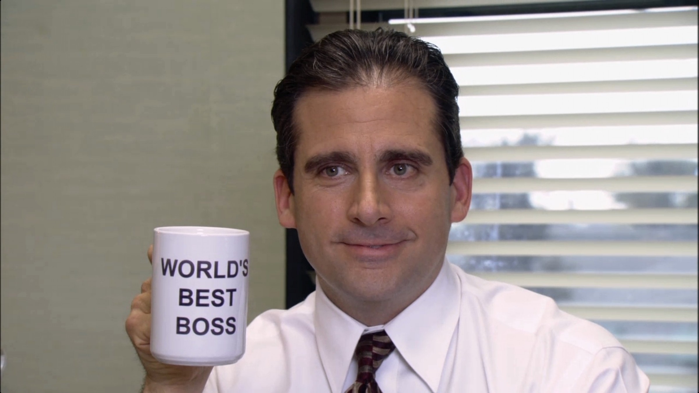 Michael Scott from The Office poses with his "World's Best Boss" coffee mug.