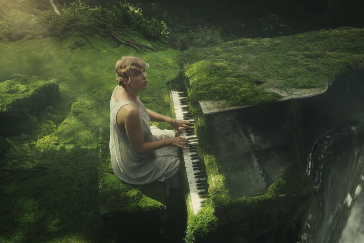 Taylor Swift sitting in a nightgown at a piano that's covered in moss for the "cardigan" music video.