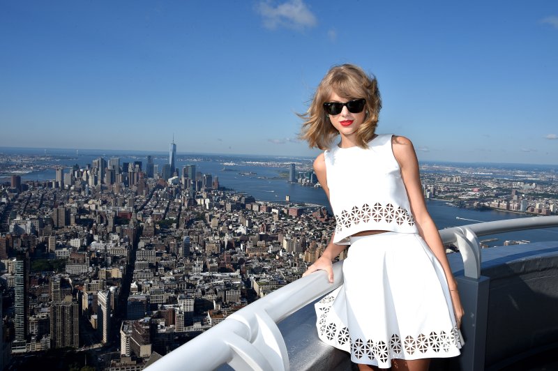 Taylor Swift, standing above the NYC skyline from a balcony that is presumably the Empire State Building.