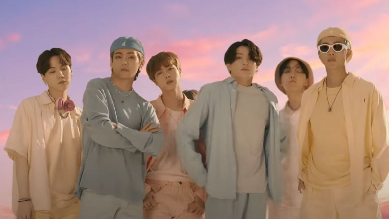BTS standing in front of a colorful sky in their Dynamite music video.