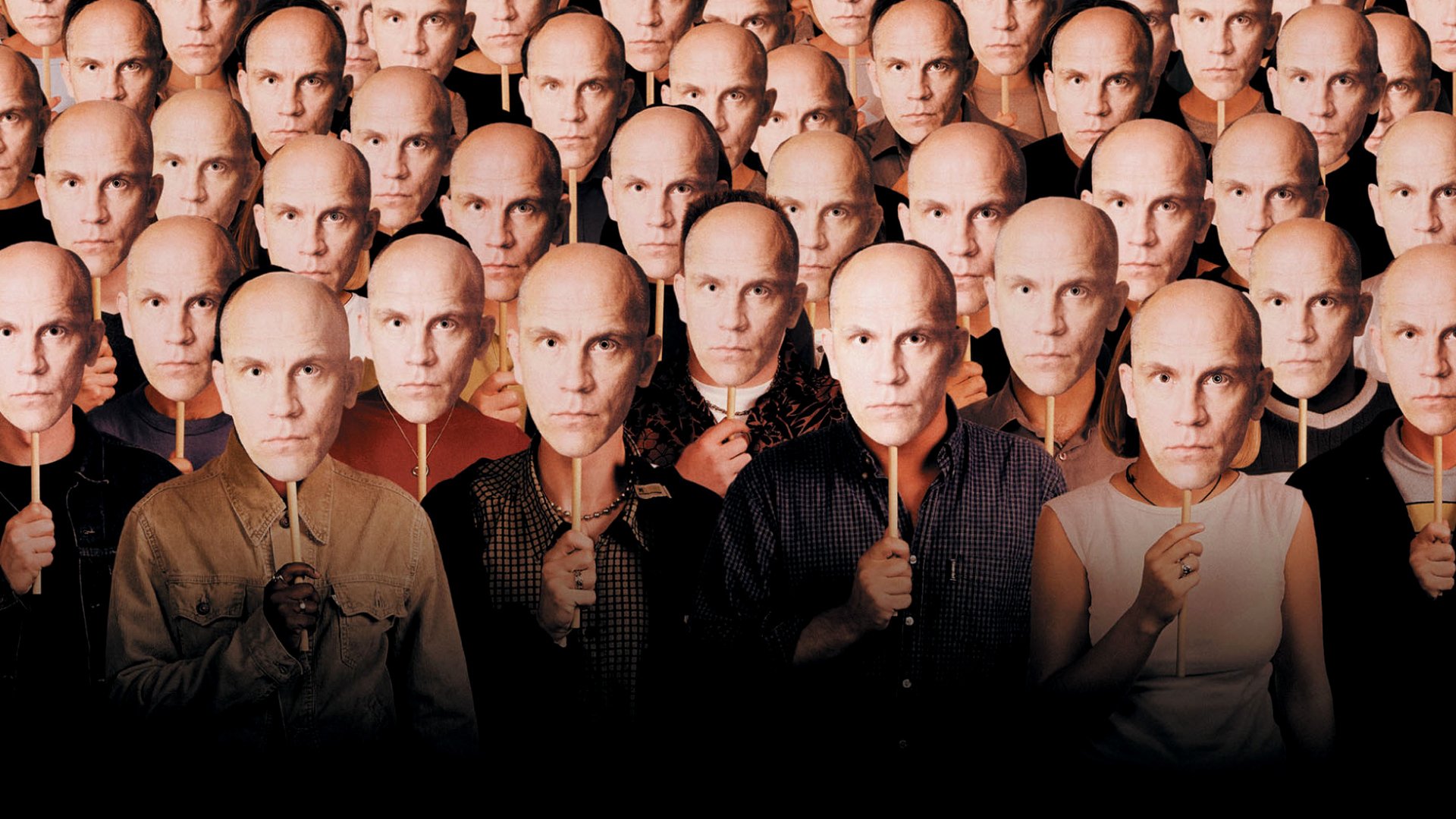 Audience members in Being John Malkovich hold Malkovich masks to their face. 