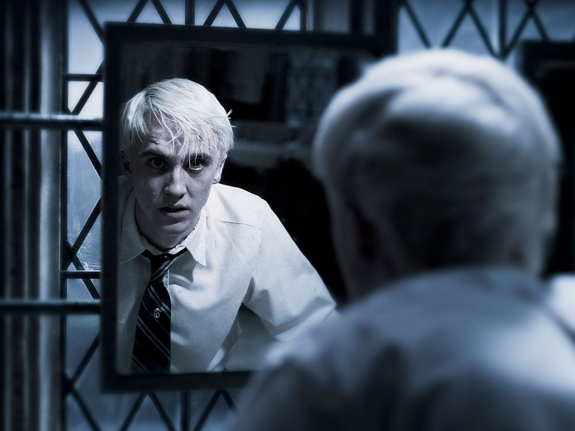 Draco Malfoy stares at himself in the bathroom mirror with a scared expression on his face.