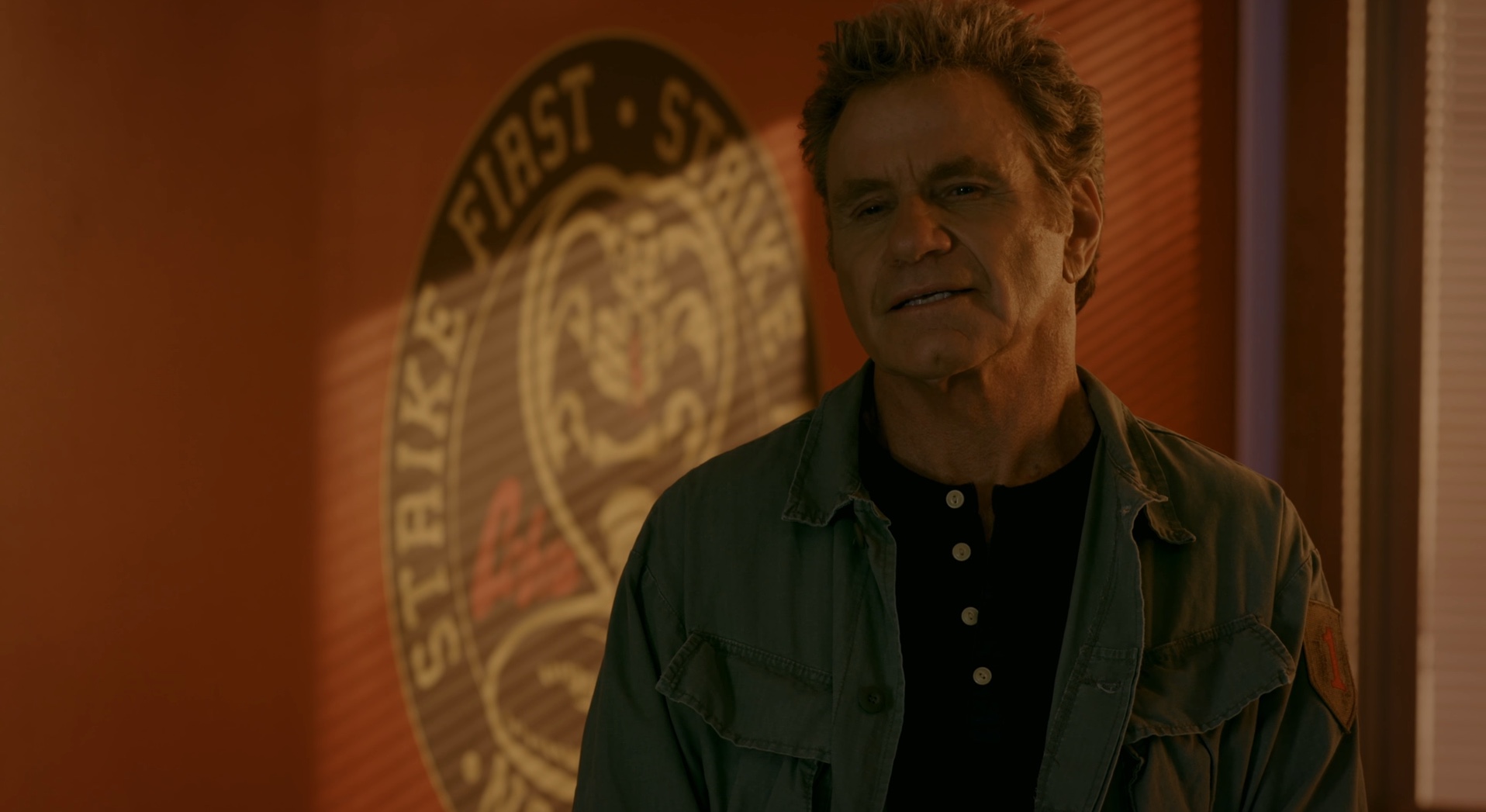 John Kreese stands in the Cobra Kai dojo in the evening light.