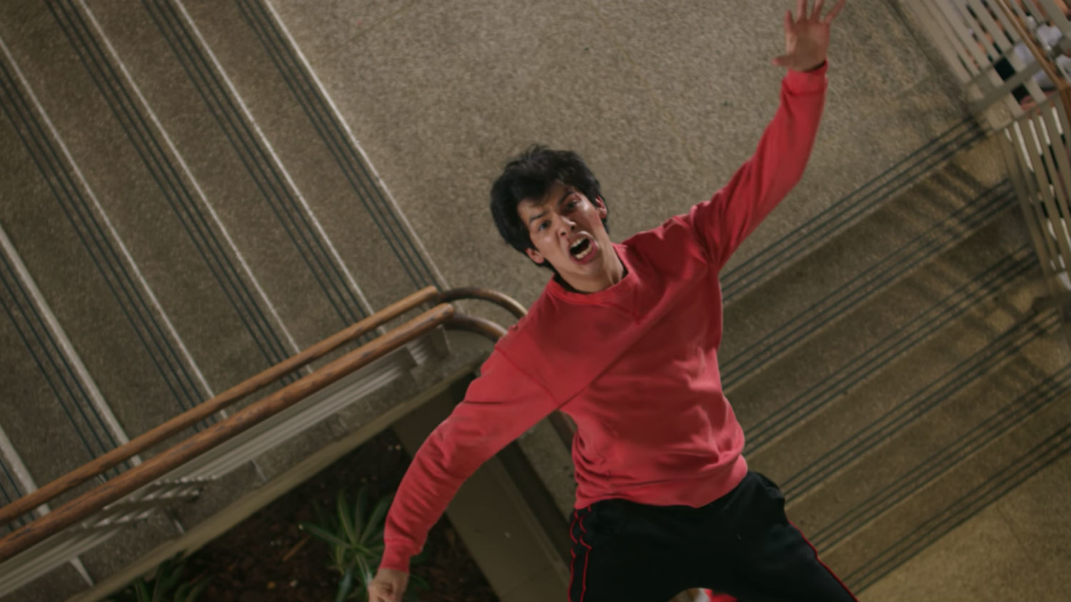 Miguel, clad in a red sweater, is mid-fall above the stairs.