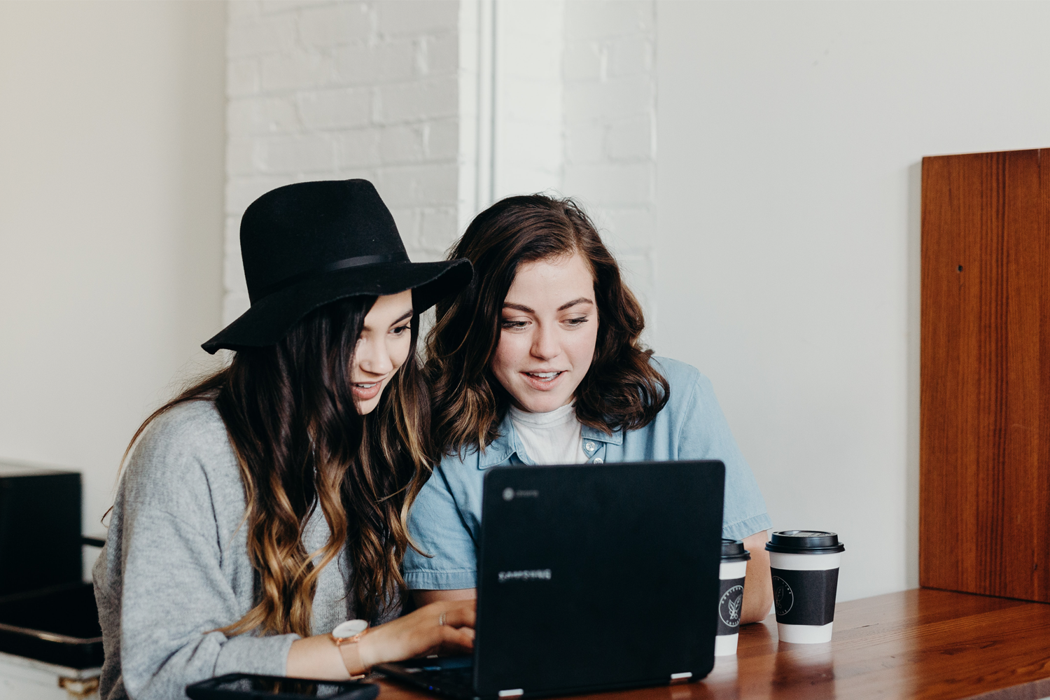 Two girls sitting near a table that are looking at a laptop.