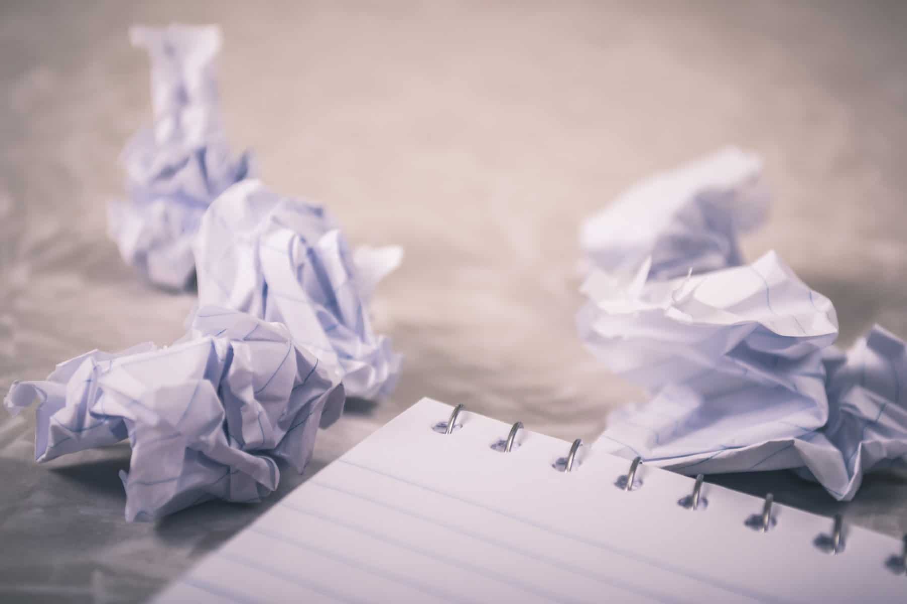 Crumpled pieces of lined paper beside a spiral-bound notebook.