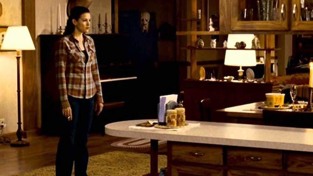 From The Strangers, a movie that will result in sleepless nights, the woman, Kristen, smoking in her kitchen while one of the murderers lurks behind her.