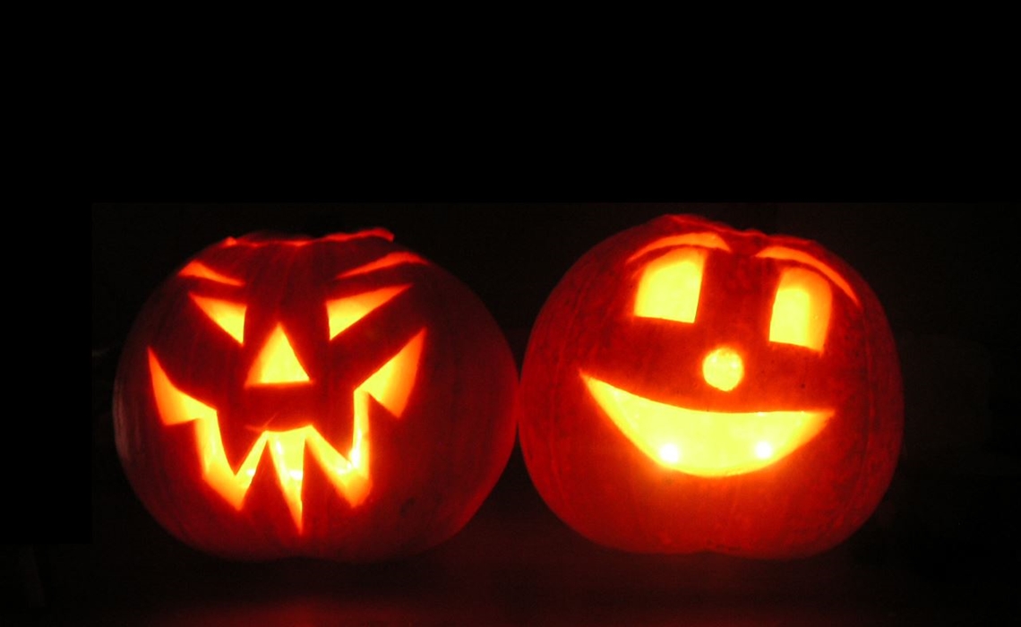 Two pumpkins sit next to each other, carved into jack 'o lanterns with lights inside them.