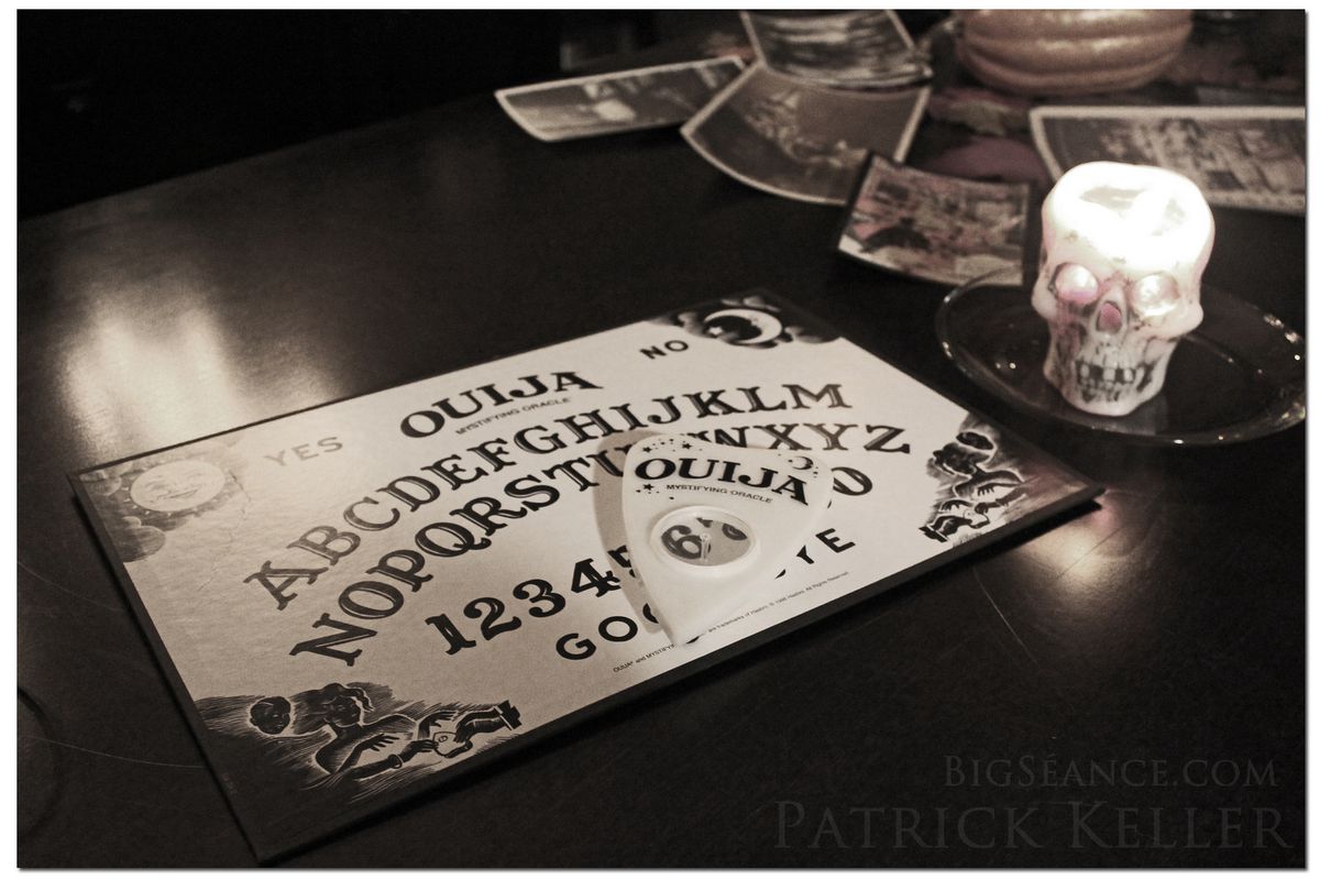 This Ouija board is on a table with candles and tarot cards around it.