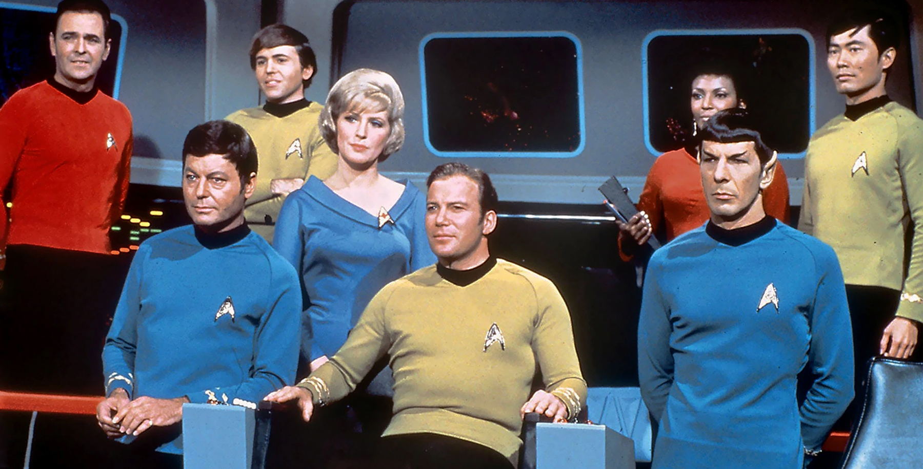 The cast of the original Star Trek stands on the bridge of the Enterprise and gazes into the distance.