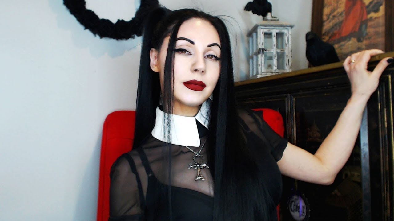 Goth woman Angela Benedict sits in a red chair with her hand extended beside her in her thumbnail for the video "Influencers Are Role Models Whether They Want It Or Not."