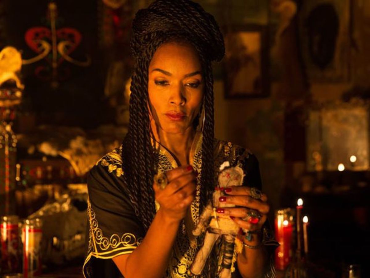 Marie Laveau holds up a pin in one hand and a voodoo doll in the other.