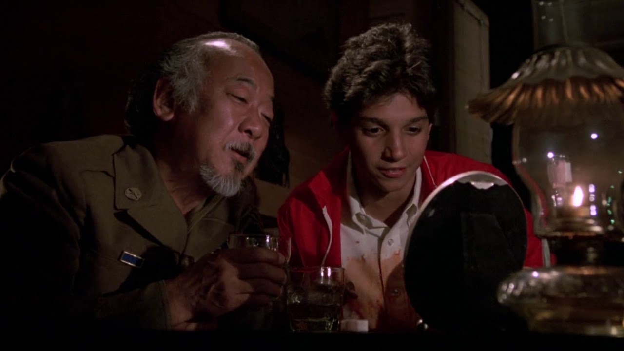 A young Daniel and a drunk Mr. Miyagi look at a picture of Mr. Miyagi's deceased wife.