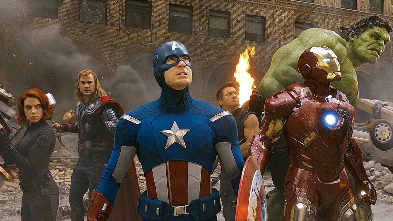 The avengers stand in a circle on a smoldering New York street, looking towards an oncoming foe.