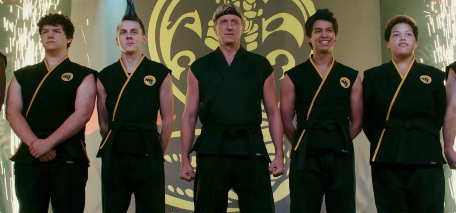 The students of Cobra Kai stand in a row, with their sensei, Johnny Lawrence, standing at the forefront of the group.