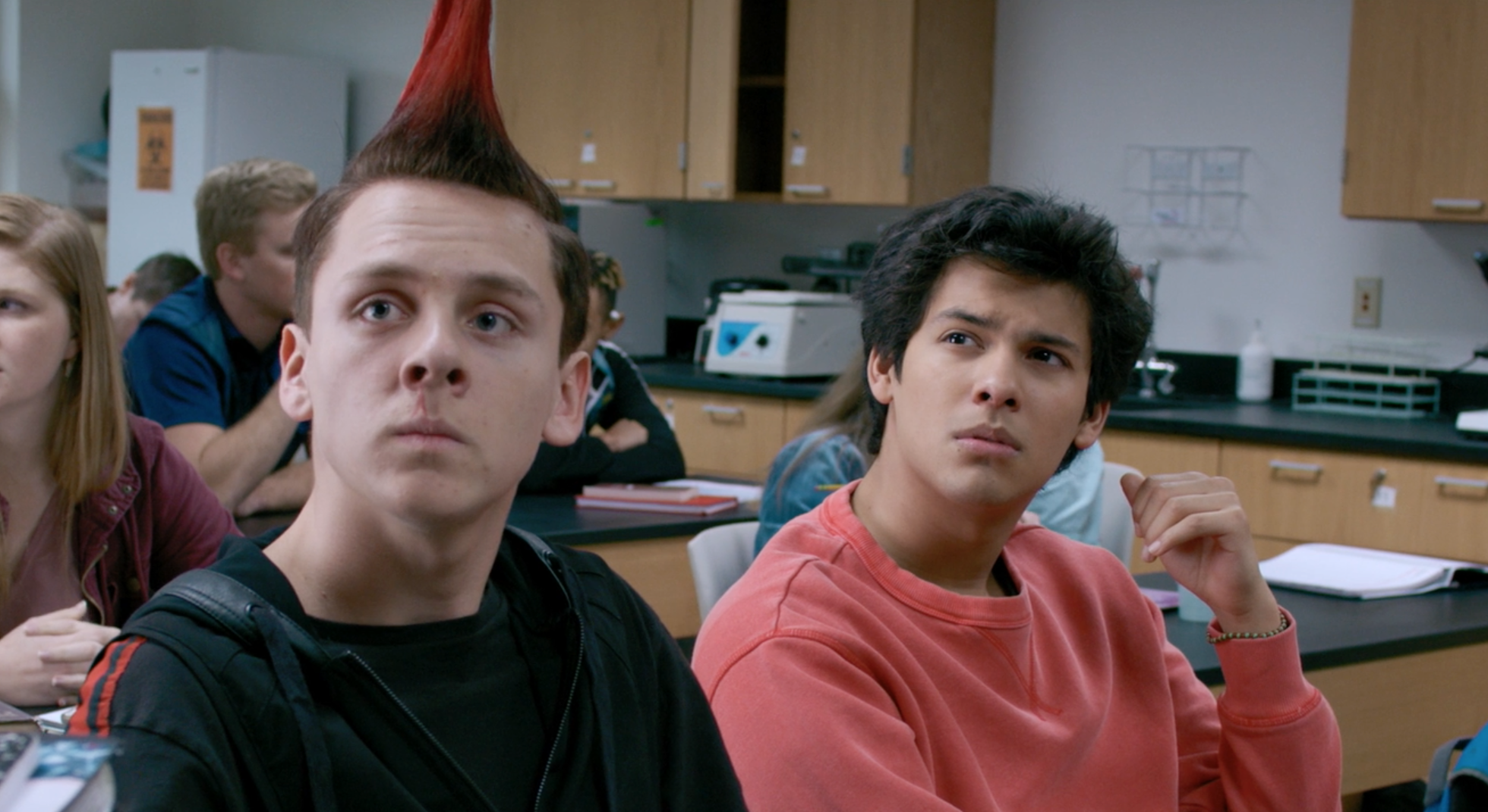 Hawk and Miguel from Cobra Kai (TV show) sit in a school classroom looking to the side.